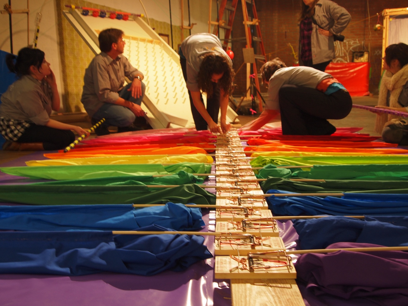 Several people crouched around a line of mousetraps running through rainbow fabric